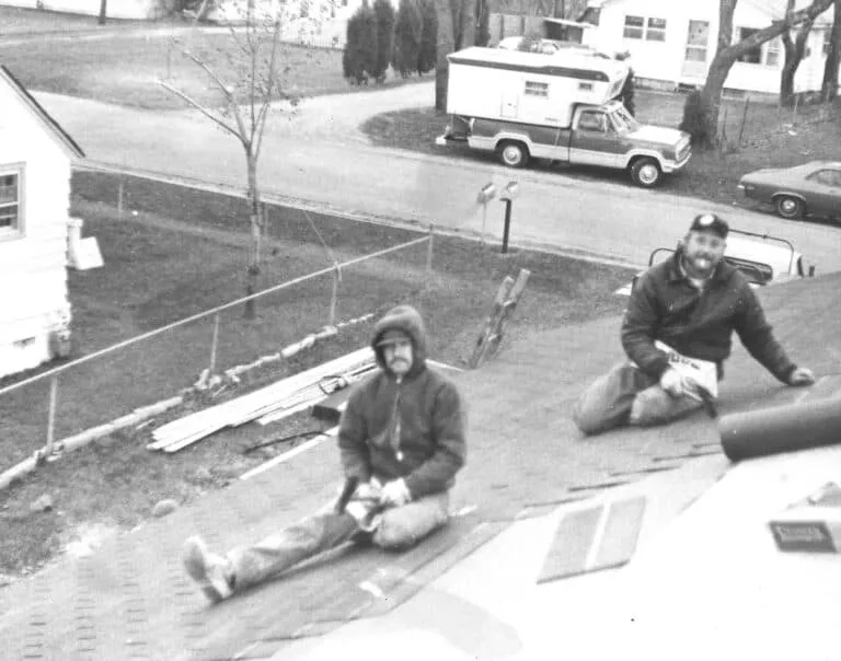 Two men sitting on a roof with aerial neighborhood view