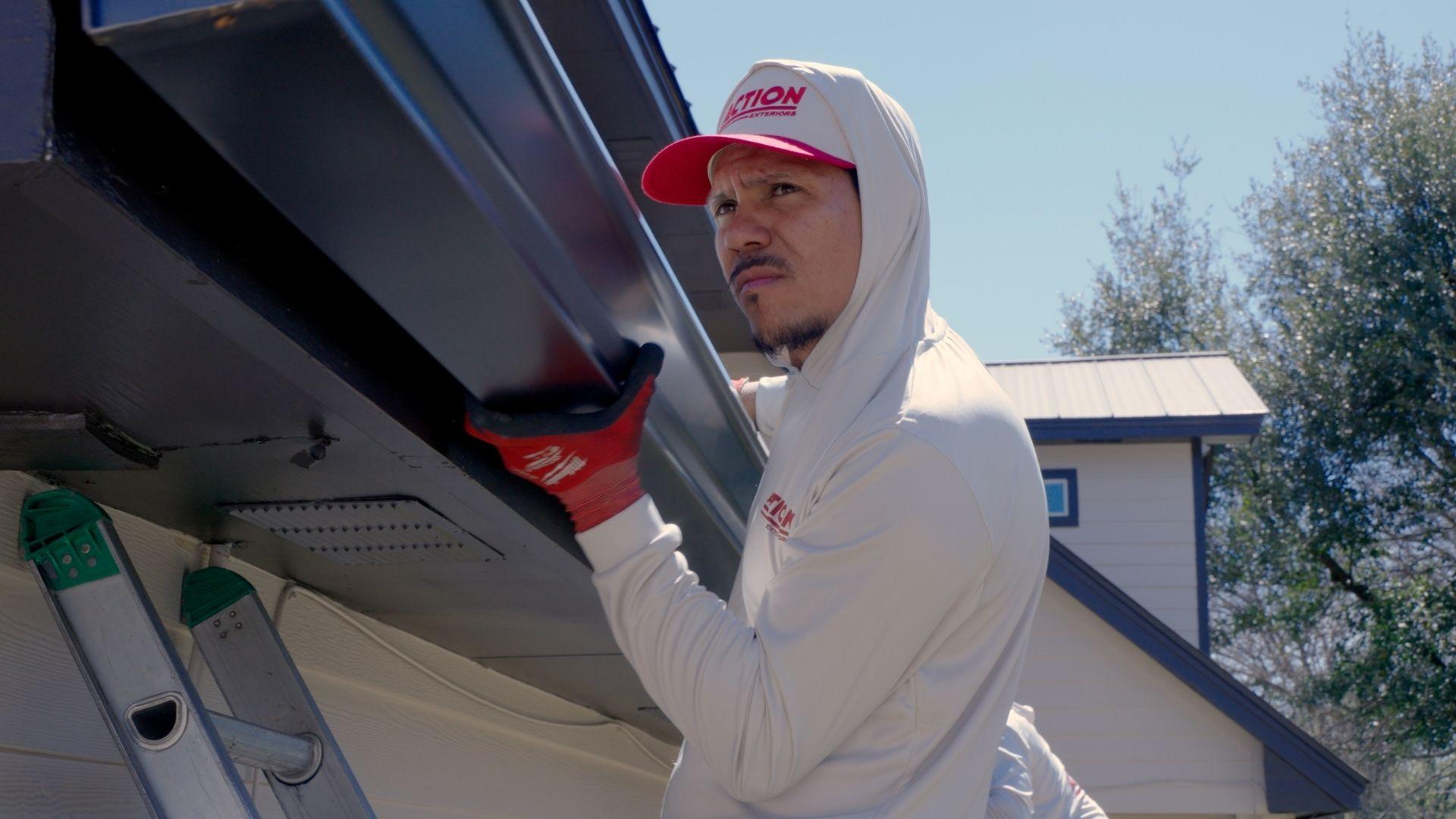 An Action Exteriors Austin employee working to install a new gutter on a roof. Roofing replacement and painting.