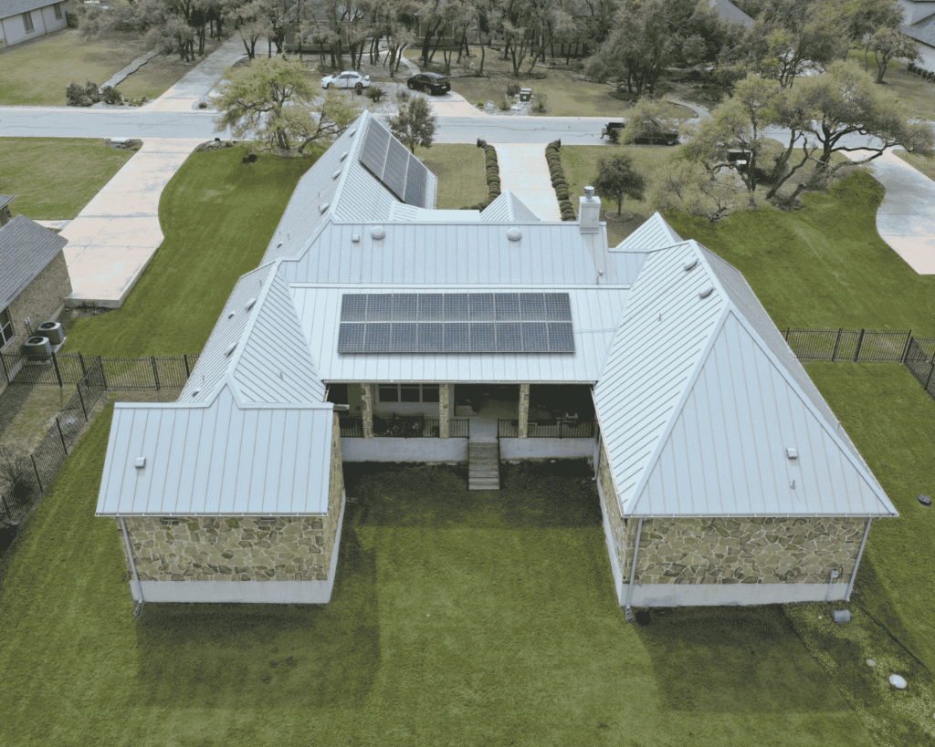 back aerial view of a beige stone home with a new silver metal roof and solar panels installed by action exteriors