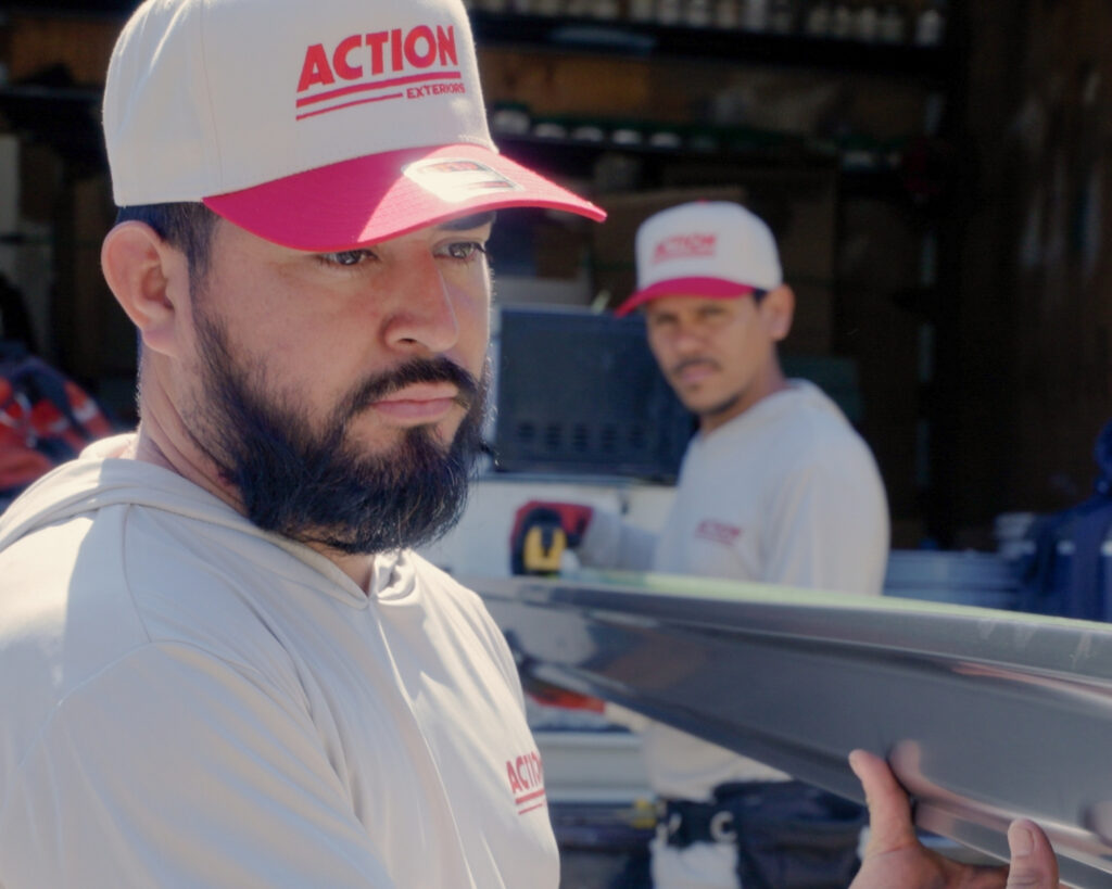two professional roofers at action exteriors carrying a large metal panel