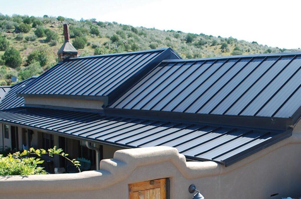 a metal roof on an adobe styled home in front of a large hill_action exteriors